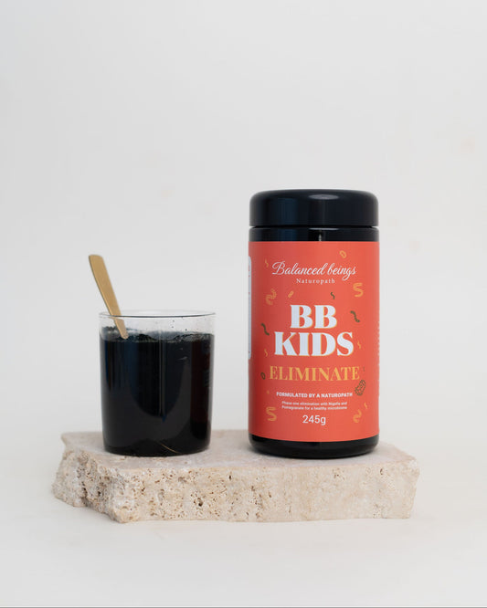 BB Kids Eliminate supplement container with a glass of dark liquid on a light surface.